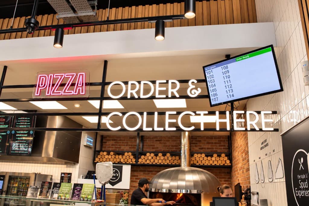 Triple 'a' Foodhall wood-fired pizza oven with roaring fire and neon Order & Collect Here signage